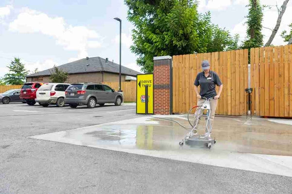 Convenience store employee using Spraymaster pressure washing system to clean drive-thru concrete, reducing labor time and improving exterior appearance